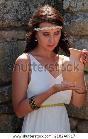 Charming smiling young woman in a Greek dress holding the old amphora on the background of the excavations of the ancient city of Nymphaeum
