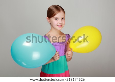 Beautiful little girl with a sweet smile, holding a yellow and blue air balloon on Holiday