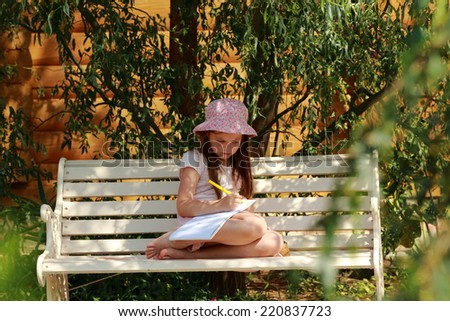 Little beautiful girl child draws with crayons in the album outdoors