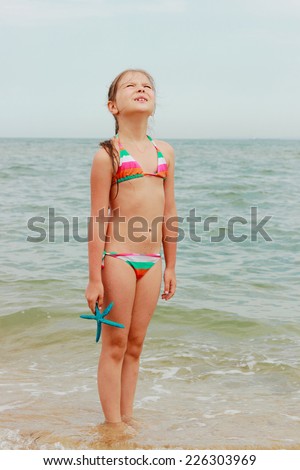 Cute little girl in a swimsuit holding a blue starfish and walks on the water on the beach
