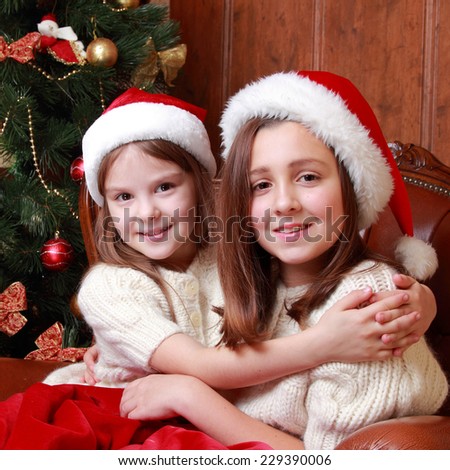 Image of cheerful little girls sitting in vintage arm chair on Christmas time on Holiday theme/Portrait of two beautiful young girls on the New Year\'s Eve and Christmas time on holiday theme