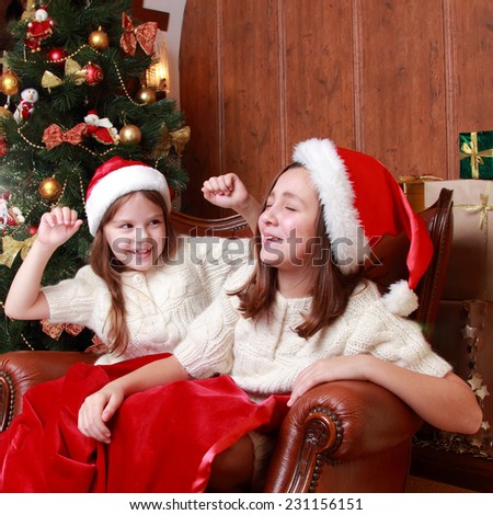 Image of cheerful little girls sitting in vintage arm chair on Christmas time on Holiday theme/Portrait of two beautifulyoung girls on the New Year\'s Eve and Christmas time on holiday theme