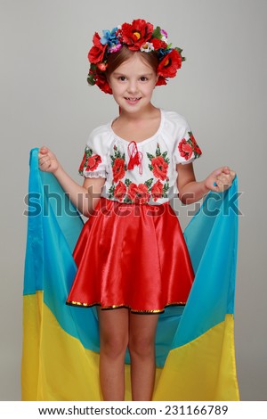 Portrait of a smiling girl in Ukrainian national headdress holding a Ukrainian flag on a gray background