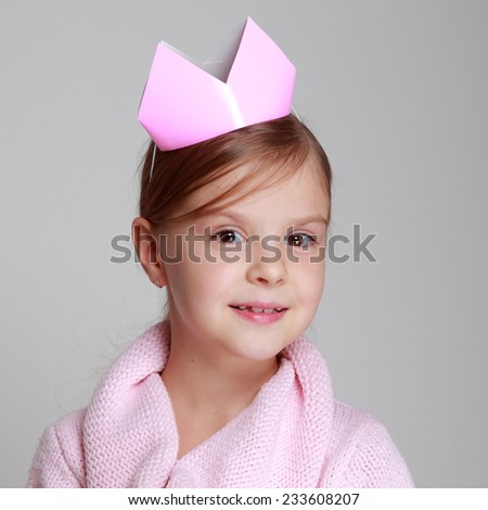 Portrait of charming smiling child in a pink knitted dress with a pink crown on her head holding a small gift on Holiday