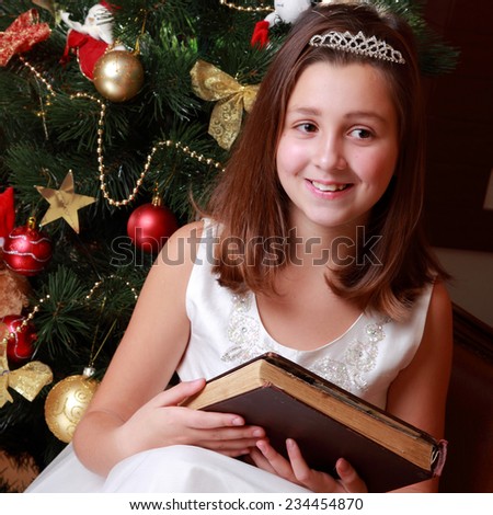 Lovely portrait of little miss santa sitting over the christmas tree and reading vintage big book on Holiday theme