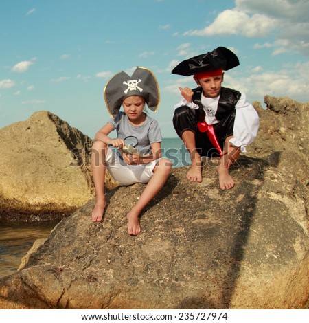 Sad boy and girl in a pirate costume and a beautiful pirate hats sitting on a large rock at the seaside/Fancy Dress Pirates