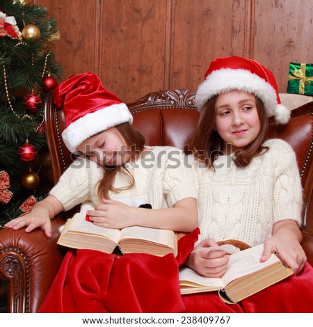 young girls sitting in vintage arm chair pretend sleeping and waiting on Santa\'s presents/Charming caucasian sisters with red and white Santa\'s hat sleeping snuggled together on Holiday theme