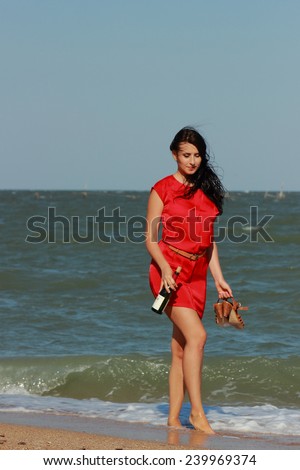 Beautiful woman walks at the sea side. Wet, red dress, high heels shoes.