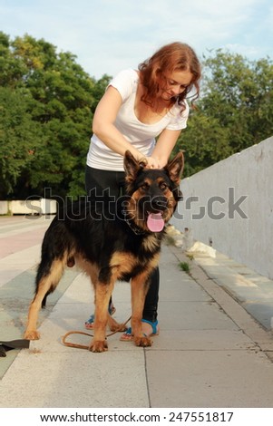 Attractive young woman brushing her dog German shepherd breed outdoor