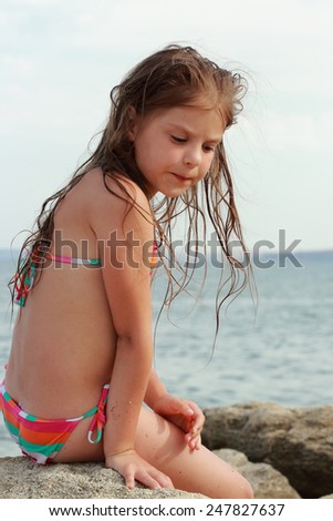 Charming little girl with a lovely smile, dreams on the beach on a summer day