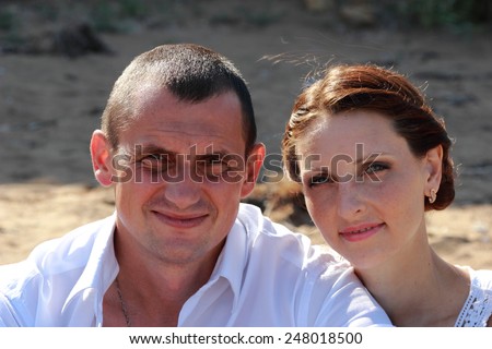 Embracing couple smiling at camera sitting on sand at the beach