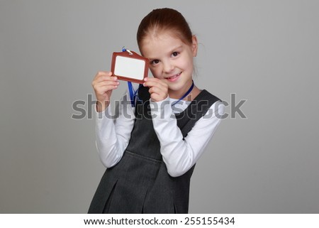 Smiling happy little schoolgirl with a blank name tag on a gray background on Education