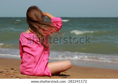 Little girl sitting on the beach with his back to the camera in summer sunny day Kerch, Crimea, Russia