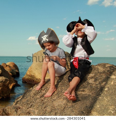 Beautiful young kids pirate boy and girl holding a pirate map and a magnifying glass looking for buried treasure on the beach