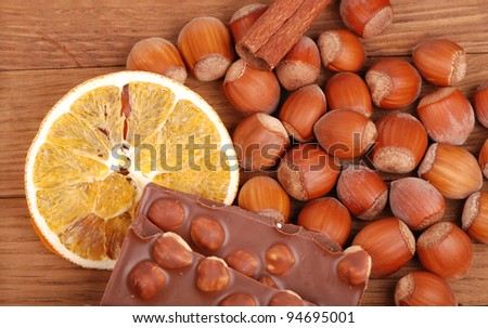 milk chocolate with hazelnuts and slice of dry orange, lots of hazelnuts and a stick of cinnamon as a background on a food and drink concept theme/spices and chocolate with hazelnuts