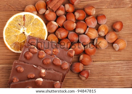bars of milk chocolate with hazelnuts and slice of dry orange, lots of hazelnuts and a stick of cinnamon as a background on a food and drink concept theme/Some spices and chocolate with hazelnuts