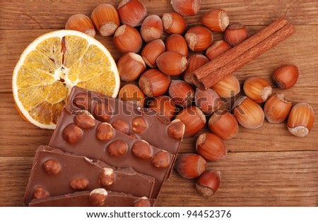 some bars milk chocolate with hazelnuts and slice of dry orange, lots of hazelnuts and a stick of cinnamon as a background on a food and drink concept theme/milk chocolate with hazelnuts