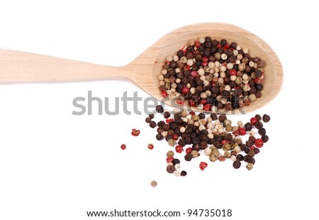 lots of ground pepper of different colors on light brown wooden spoon over white background/ground pepper
