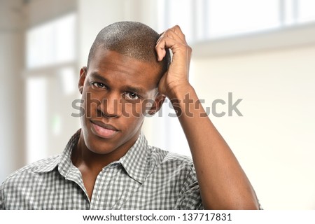 Portrait of young African American man scratching head indoors