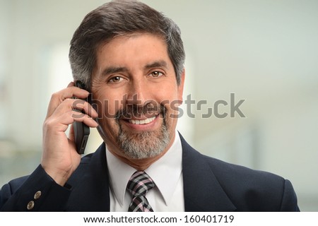 Portrait of senior Hispanic businessman using cell phone inside office building