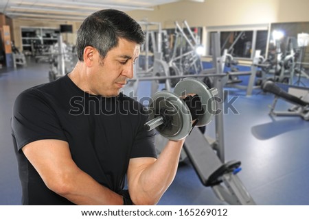 Portrait of mature Hispanic man exercising with dumbbells inside gym