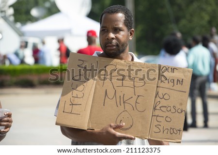 FERGUSON, MO/USA  AUGUST 15, 2014: Demonstrator holds sign at the site of destroyed Quick Trip after Police Chief Thomas Jackson release of the name of the officer that shot Michael Brown.