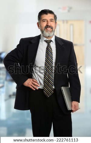 Portrait of senior Hispanic businessman holding laptop inside office building
