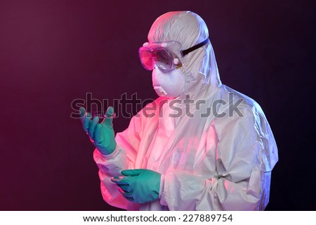Scientist in protective Hazmat suit, gloves and goggles holding petri dish