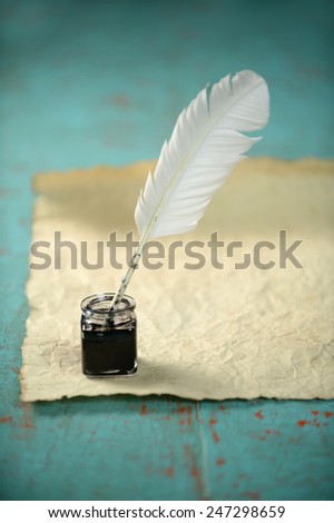 Inkwell and feather with old paper on grunge table