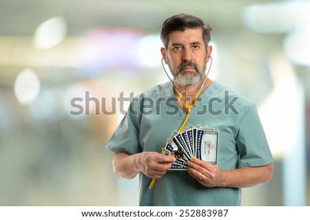 Social security concept. Senior doctor holding stethoscope to cards inside hospital building