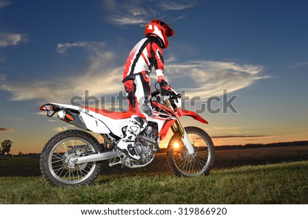 Motocross rider standing on motocycle during sunset
