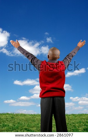 Boy with arms raised expressing joy over a blue sky with clouds.