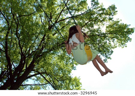 Girl on a swing flying high over a background with trees.