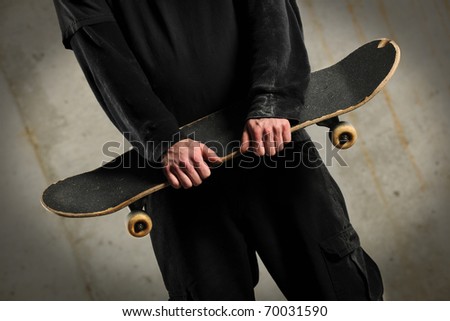 Mid section of man holding skateboard over concrete background with spotlight