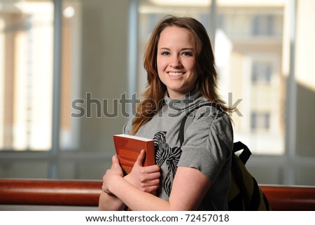 Female student smiling holding books inside building