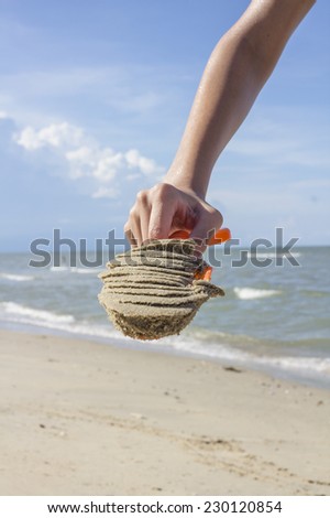 Close up hand of Asian Thai boy holding plastic shovel with sand on tropical beach at the day time