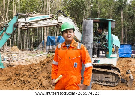 NAKHON SRI THAMMARAT, THAILAND - MAY 10: Thai worker wearing high safety jacket standing and watching bucket digger digging at construction site on May 10, 2015 in Nakhon Sri Thammarat, Thailand.