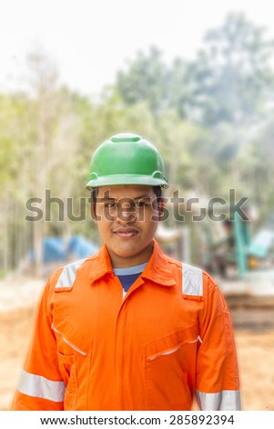 Thai construction site worker wearing high visibility safety jacket standing and watching paper