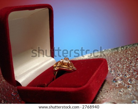 beautiful ring in box on blue and silver background with drop of water