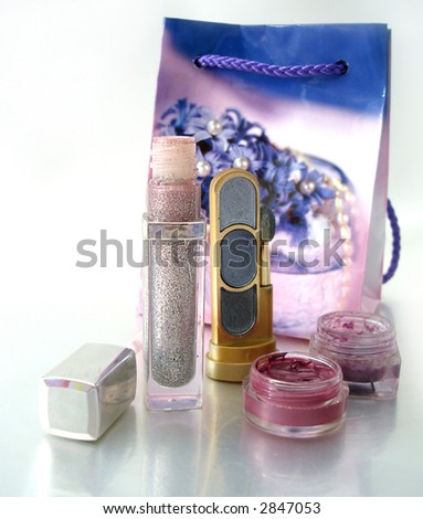 Detail of assortment of makeup (blue eyeshadows, silver gloss for lips,  two lipstics) and bag