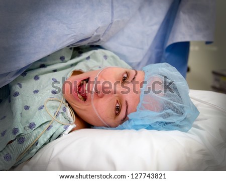 A woman in surgery with a wide eyed open mouthed frightened look on her face.