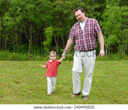 Father and Son walking towards the camera.  Son is holding a dandelion.