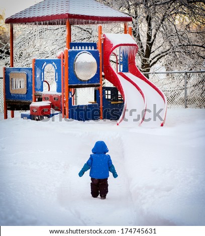 Small child looks longingly at the local playground which is dangerously covered in snow and ice. Wishing it was spring when it will be again safe to play on it.