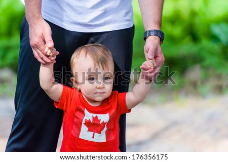 Toddler in Canada Flag shirt walking assisted by his father. Room for copy space.