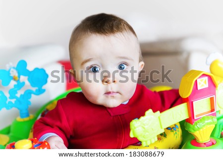 A wide eyed baby boy in a walker or jumper pauses to look at the viewer.