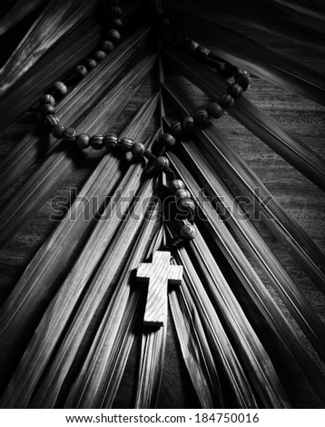 Palm Sunday still life - A beaded olive wood cross or rosary rests upon a palm branch on top of a rustic table.  Presented in Black and White.