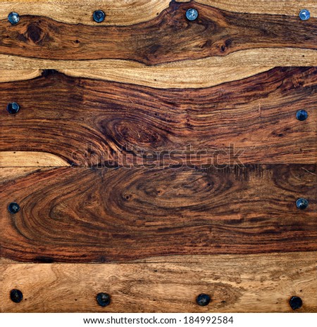 Surface of a rustic wooden table or wooden background, bordered with hand hammered wrought iron nails or rivets.