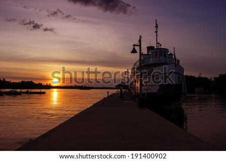 A ship is docked at a wharf during sunset on a lake.