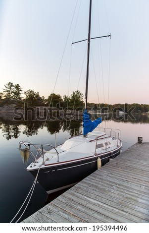 A small sailboat sits docked on a calm lake during the evening.