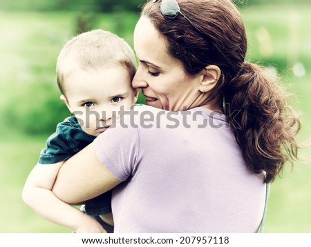A happy mother holding a toddler with a sad expression.  Filtered for a retro vintage look.